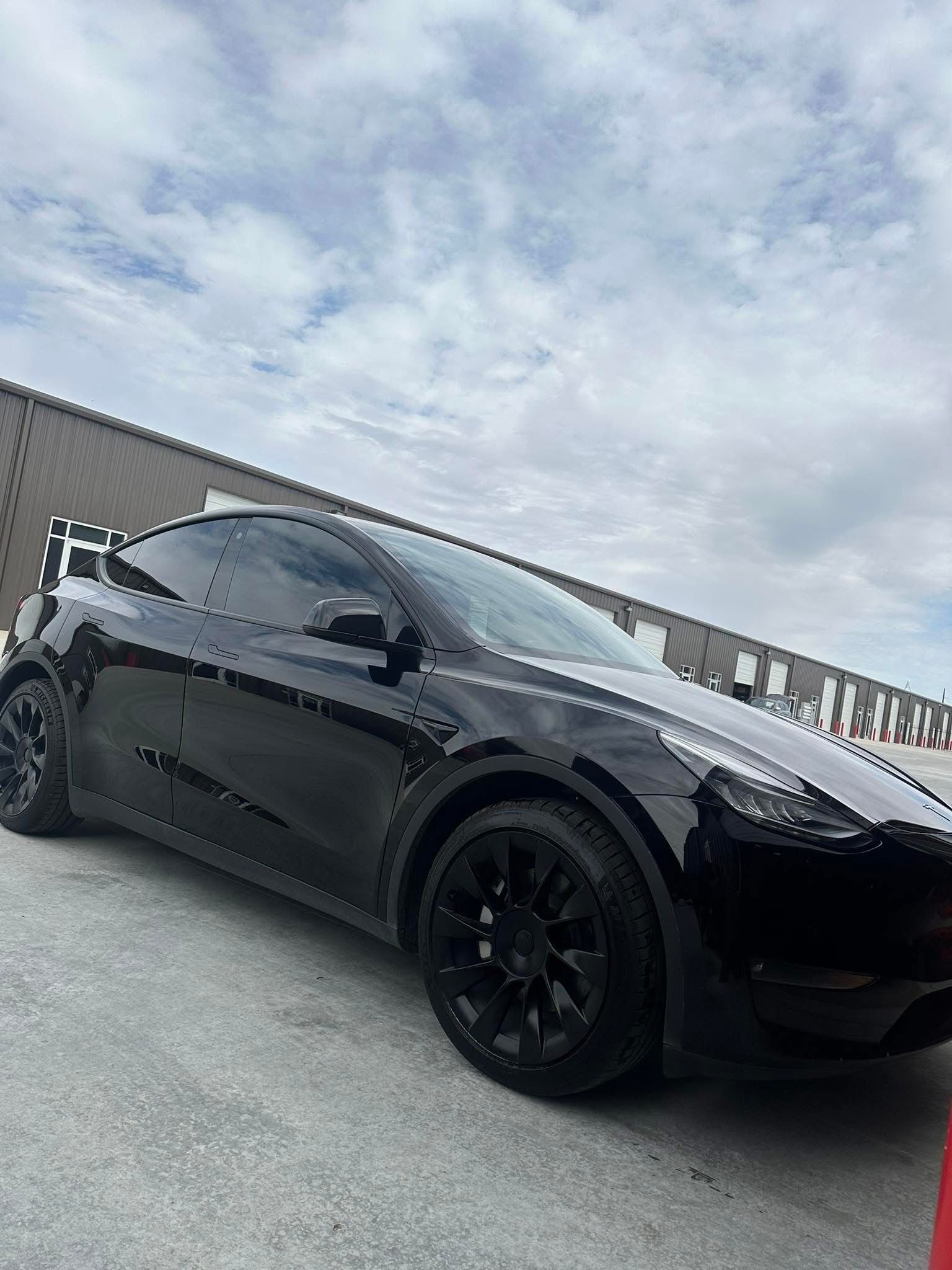 Black Tesla Model Y parked in front of a building with a cloudy sky in the background.