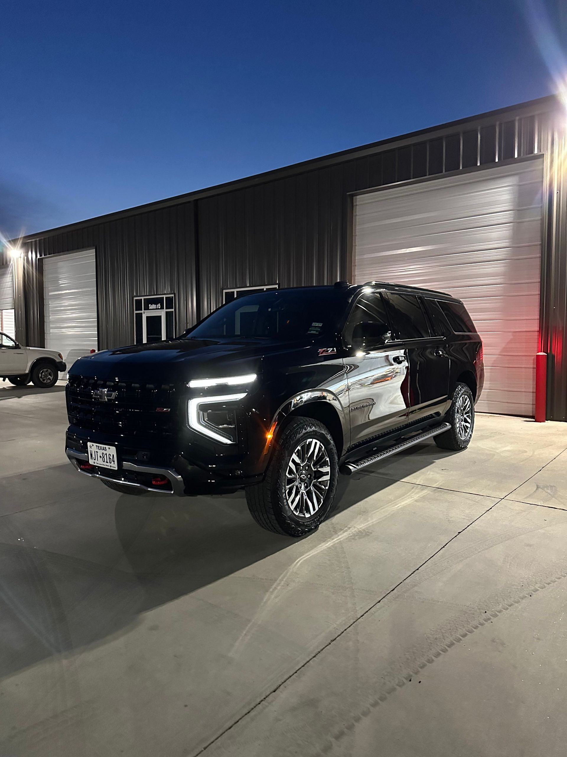 Black Chevrolet Tahoe SUV parked in front of a building with overhead doors, under dim lighting.