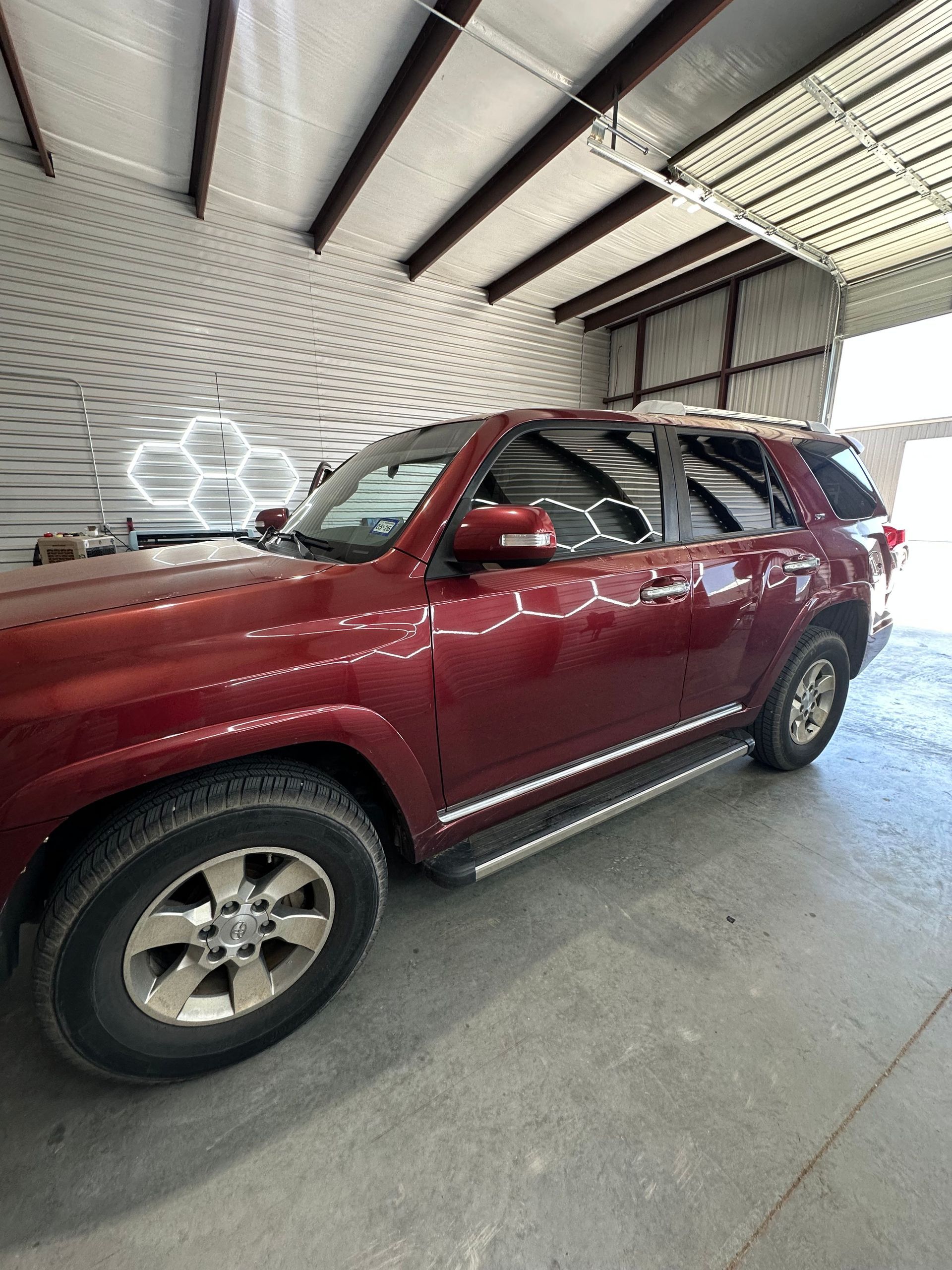 Red SUV parked inside a well-lit garage, with a white honeycomb-shaped light fixture in the background.