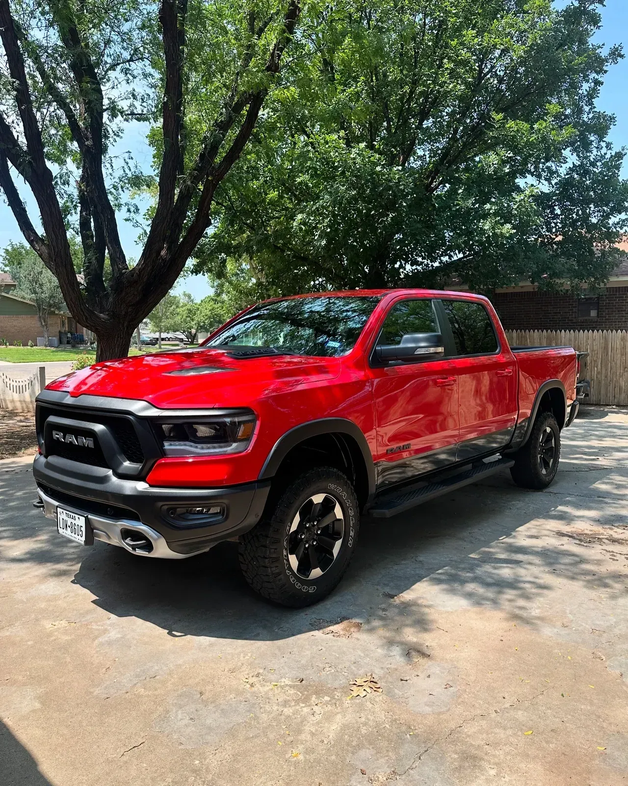 Red Ram Rebel pickup truck parked on concrete driveway near a tree.
