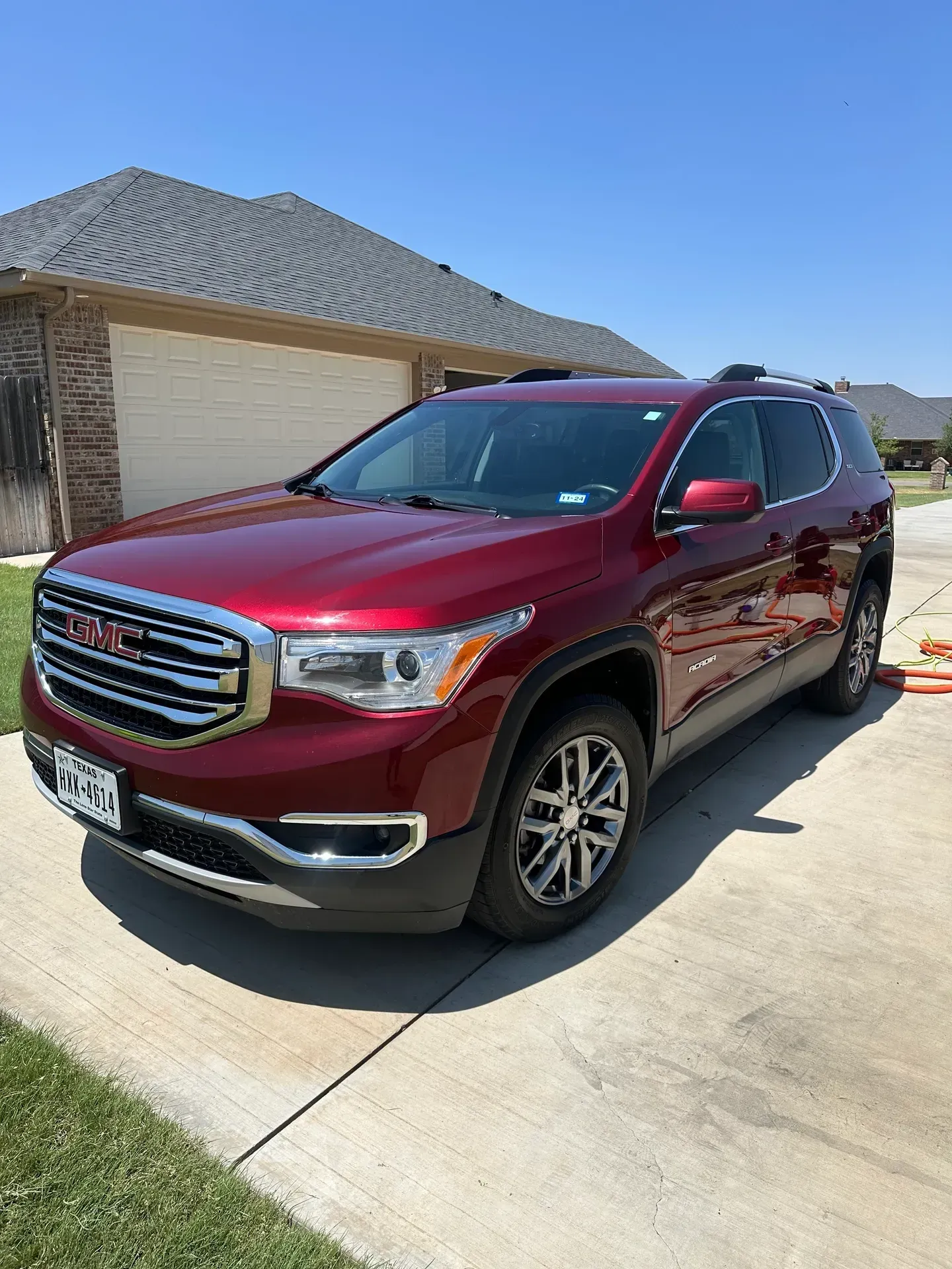 Red GMC Acadia SUV parked on a concrete driveway in front of a house.