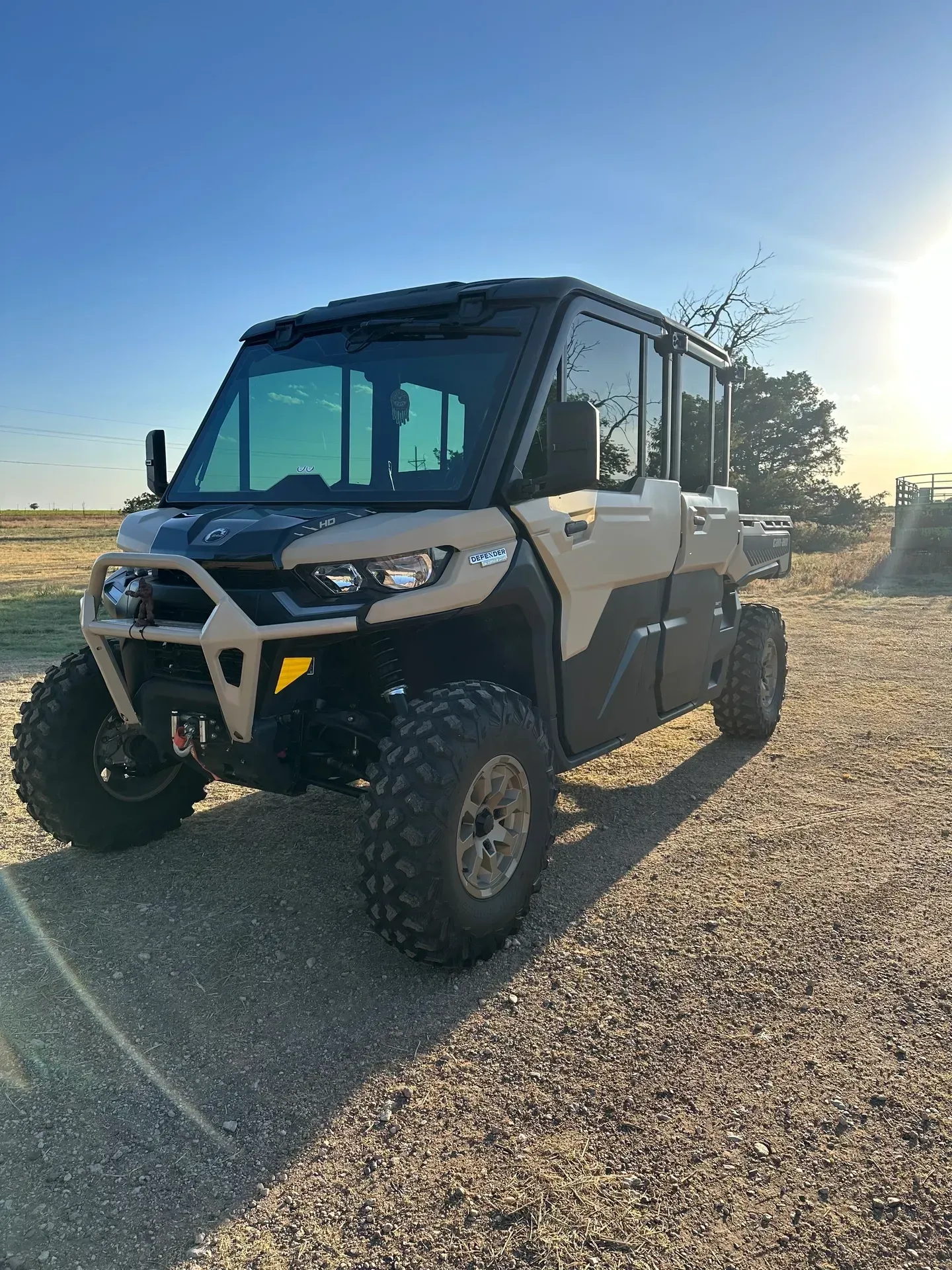 Off-road utility vehicle with beige and black accents, parked on gravel in bright sunlight.