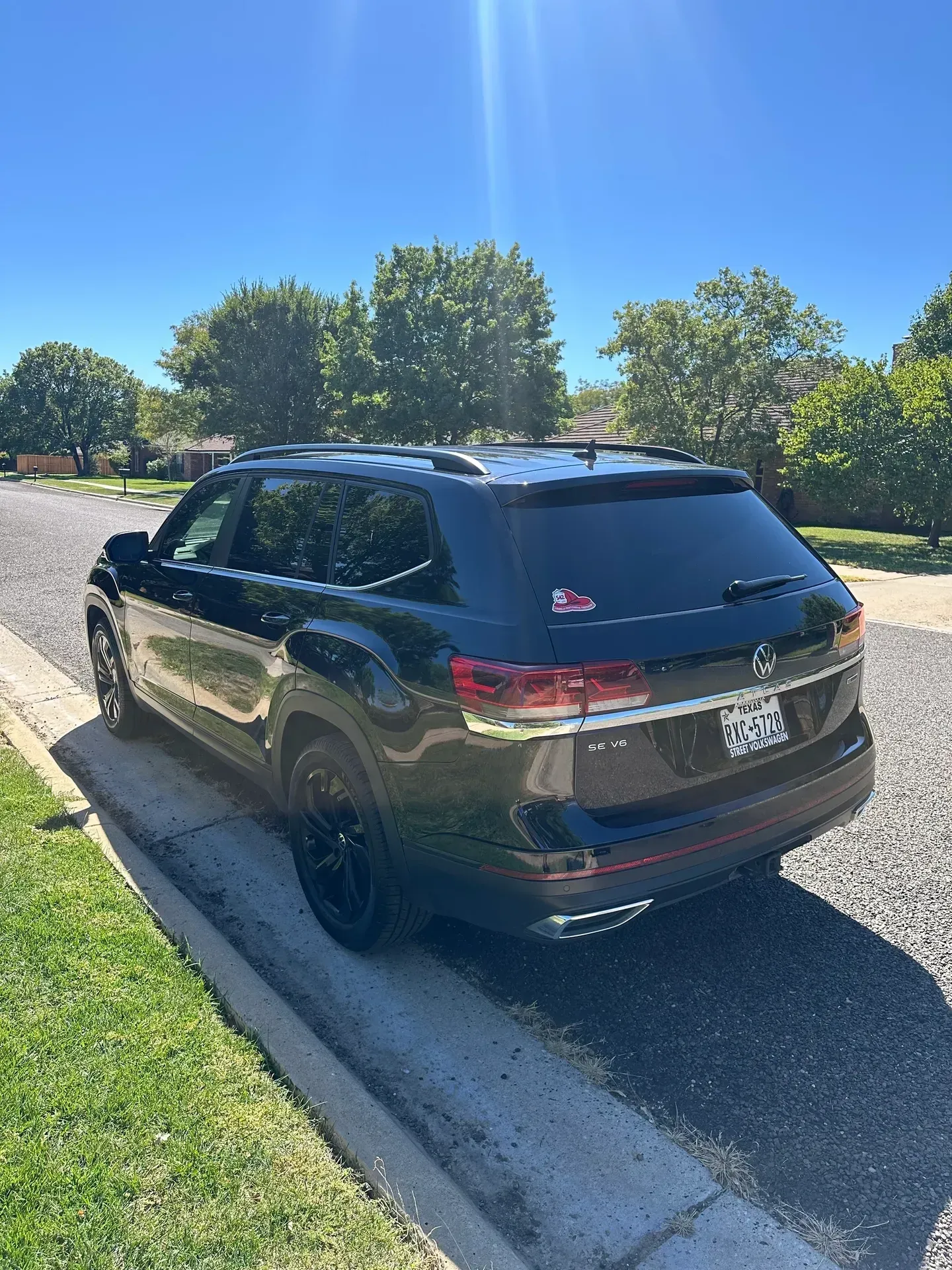Black Volkswagen Atlas SUV parked on a gravel driveway next to a grassy curb on a sunny day.