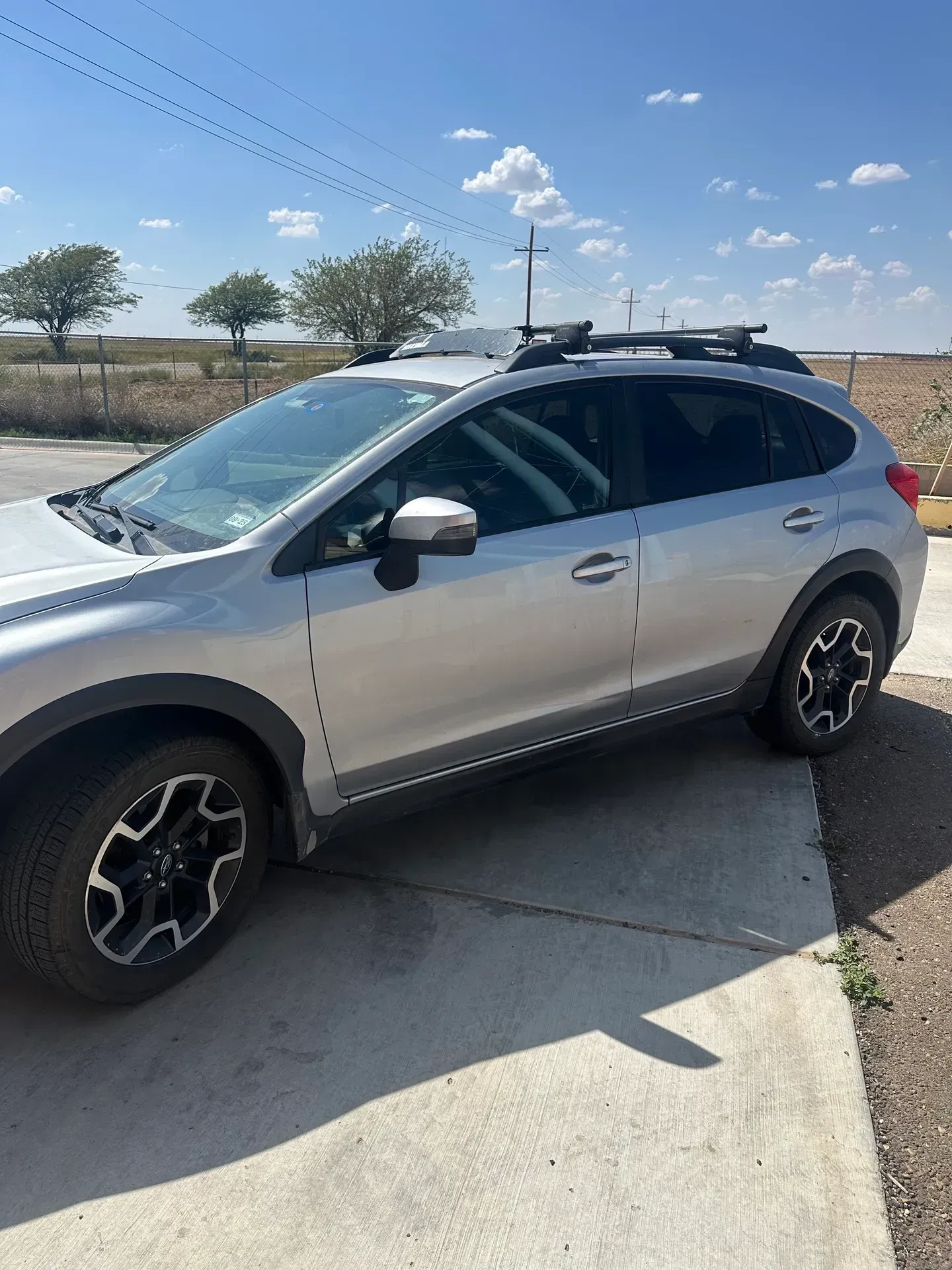Silver Subaru Crosstrek parked on a concrete driveway, under a clear, sunny sky.
