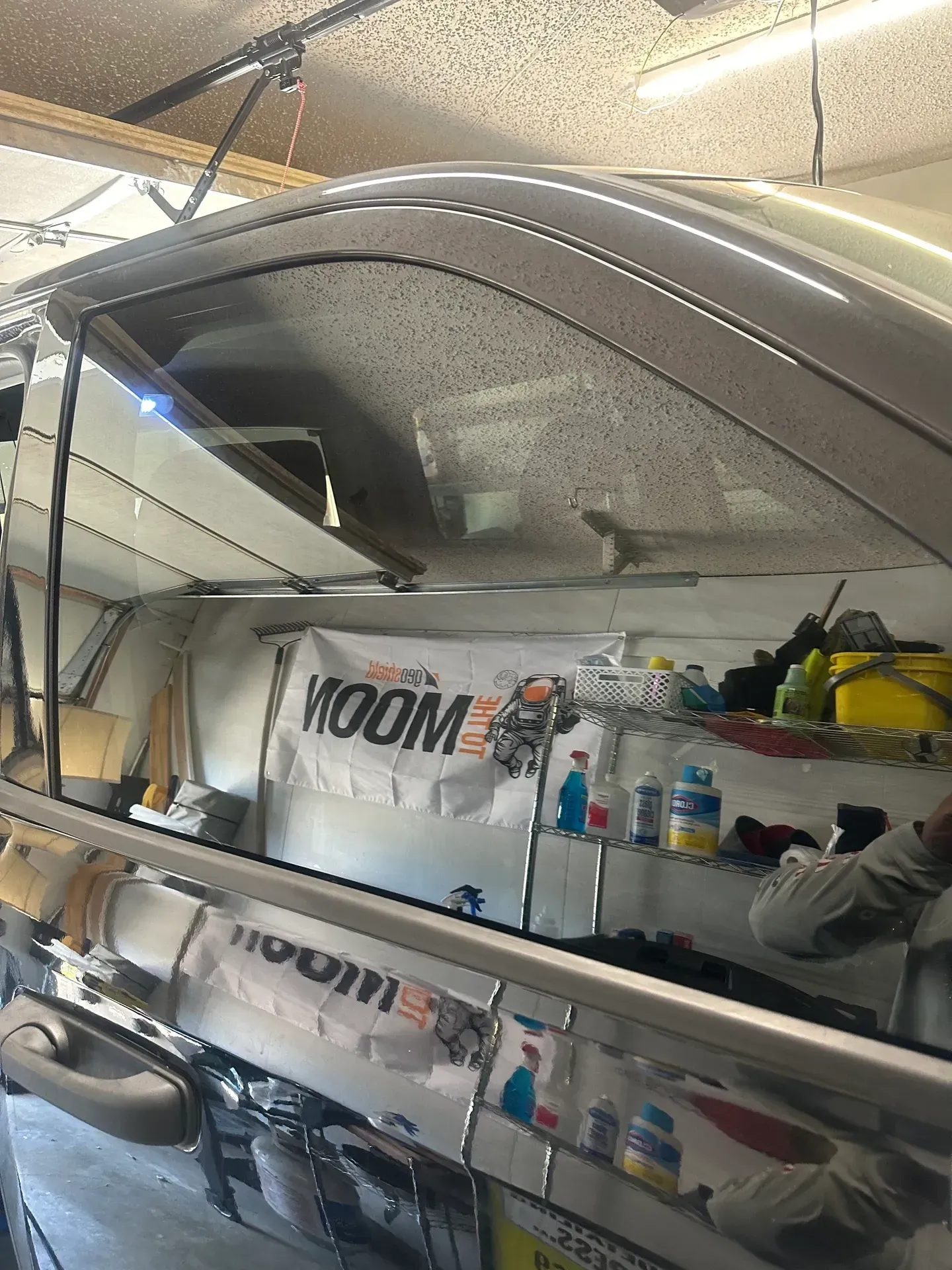 A black car window is open in a garage, revealing a cluttered interior with a banner that reads 