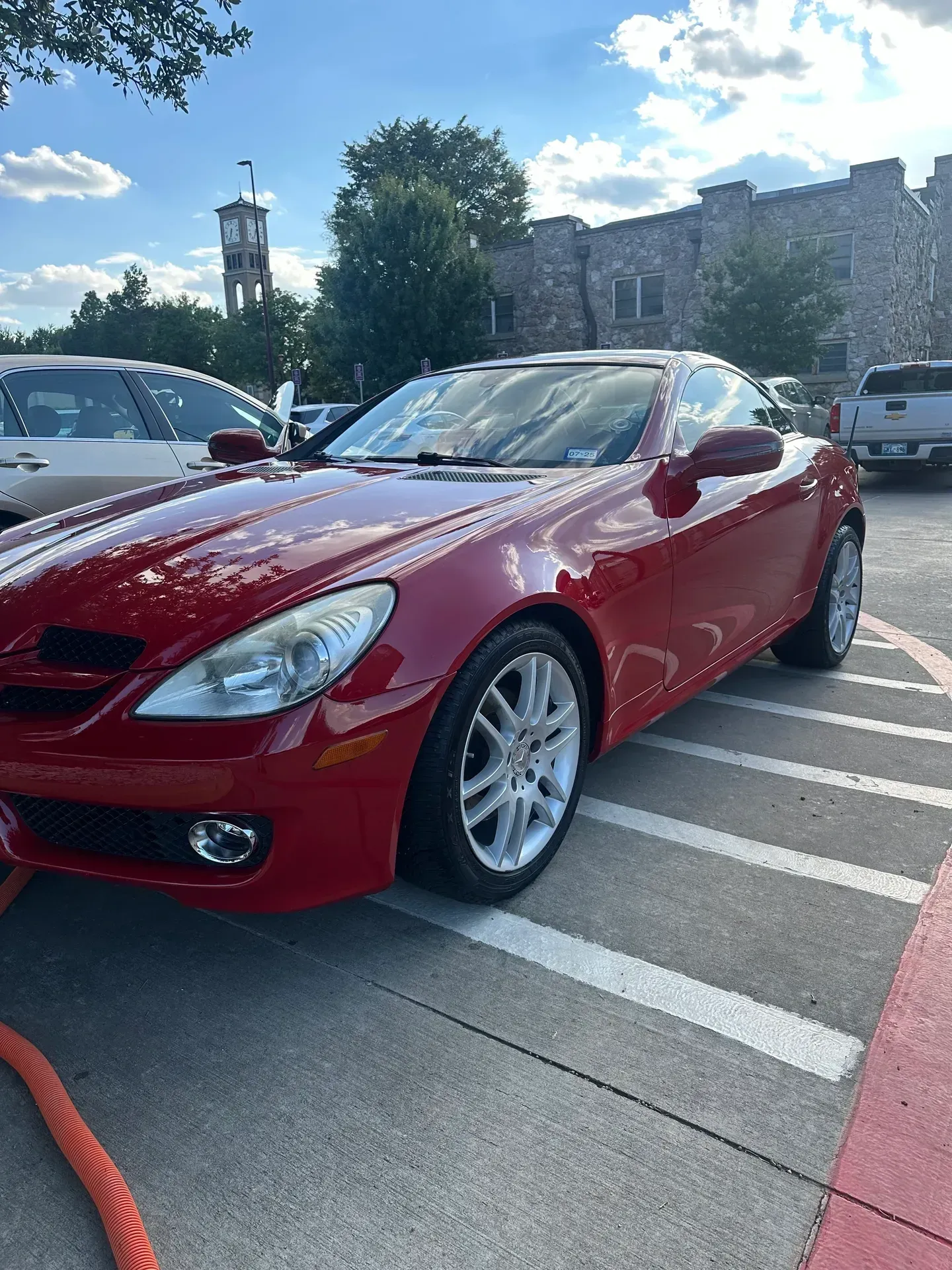 Red Mercedes convertible parked on a brick-lined surface with a building in the background.