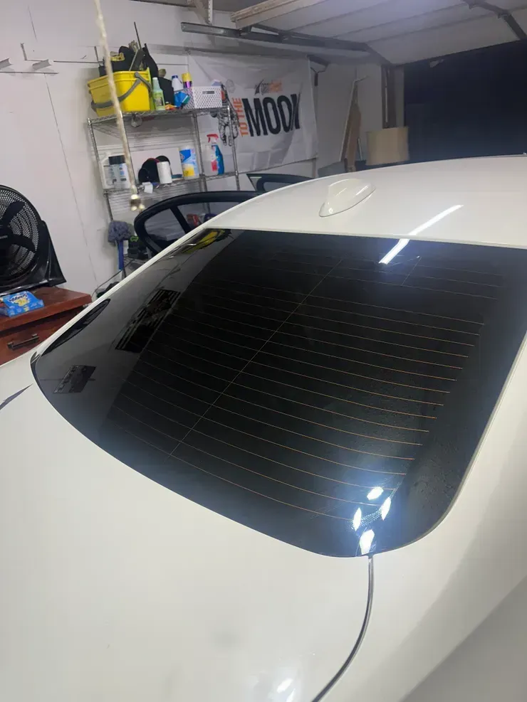 White car's rear window with dark tint, garage setting. A NASCAR flag in the background.