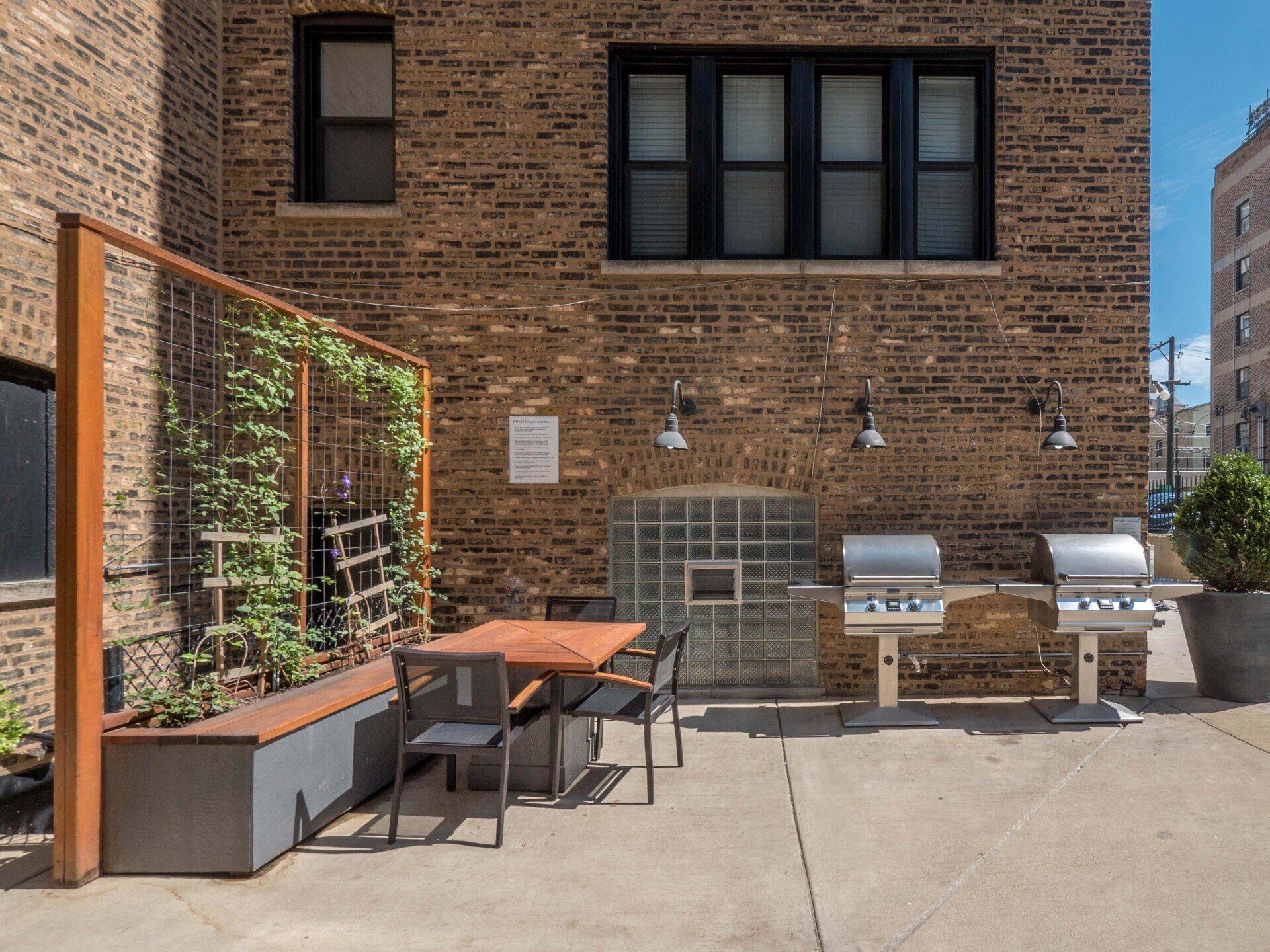 A brick building with a table, grills, and chairs in front of it at Reside on Irving Park.