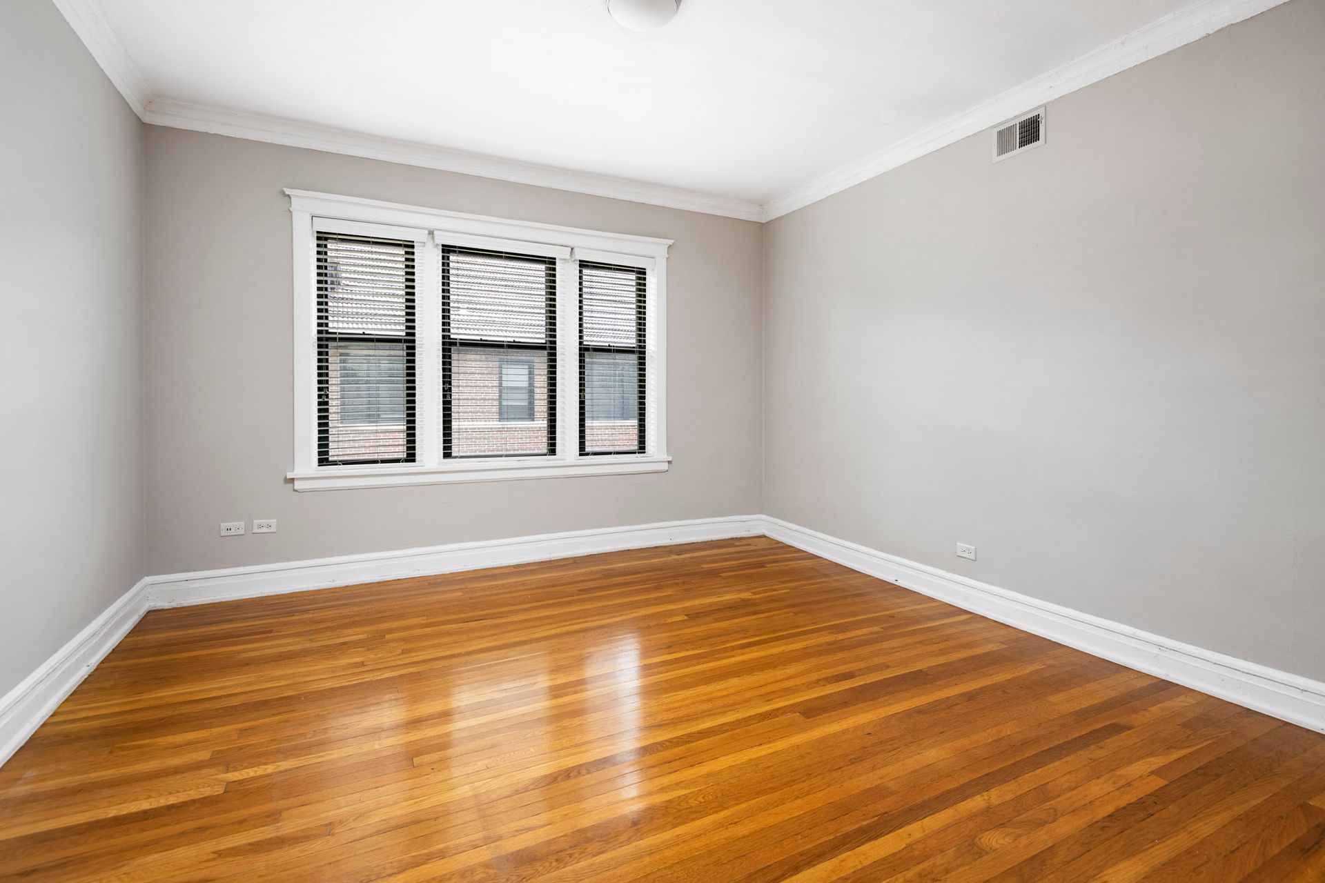An empty room with hardwood floors and two windows at Reside on Irving Park.