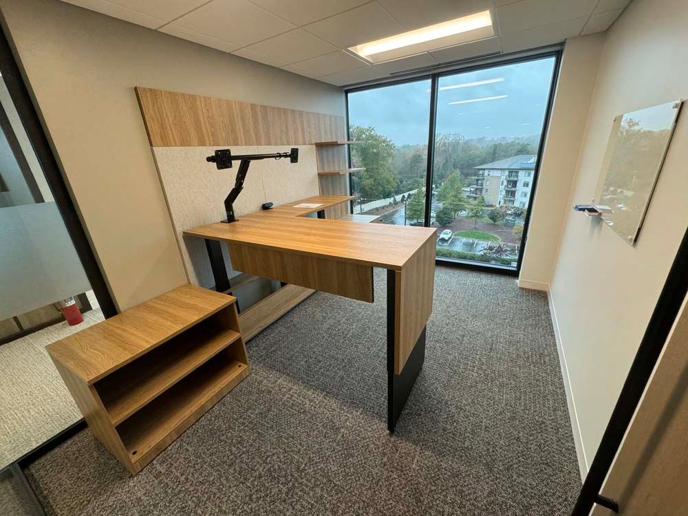 There is a desk in the middle of the room with a large window.