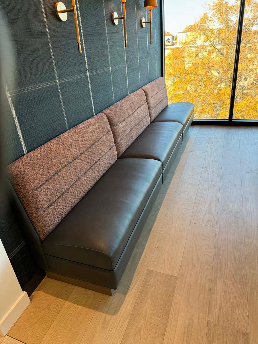 A long black couch is sitting in a room next to a window.