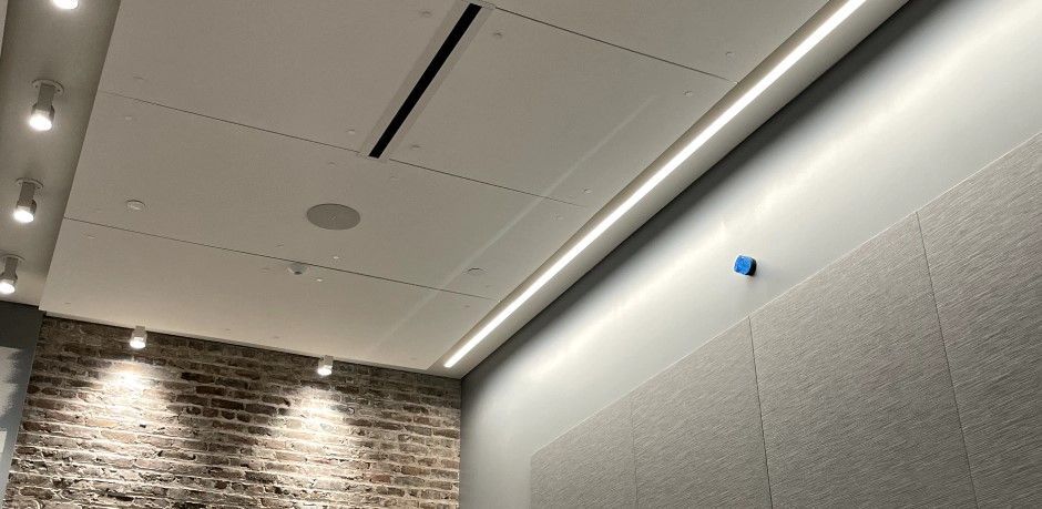 An interior ceiling with recessed lighting and a brick wall. A linear light runs along the wall.