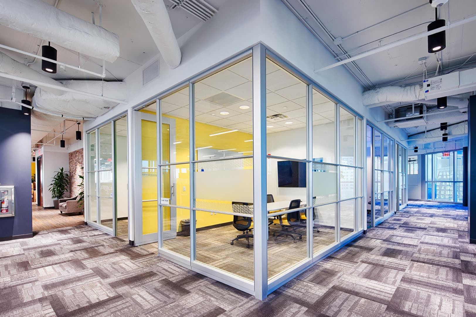Modern office interior with glass-walled conference room, open hallway, and patterned carpet.