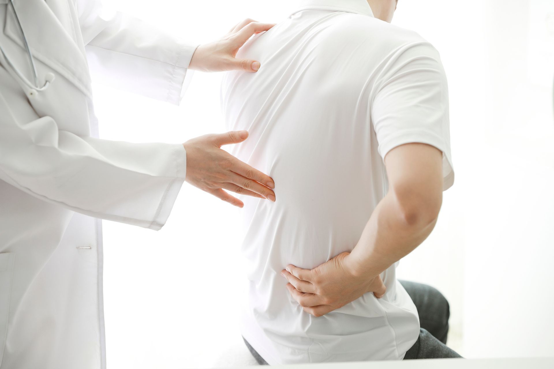 A doctor is examining a man 's back while he has a backache.