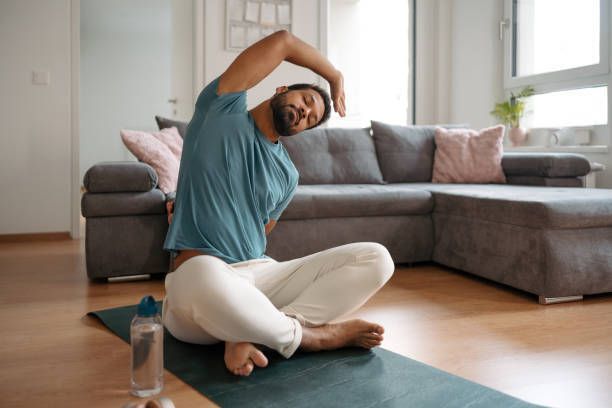 A man is sitting on a yoga mat in a living room.