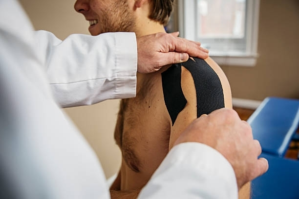 A doctor is putting kinesio tape on a man 's shoulder.