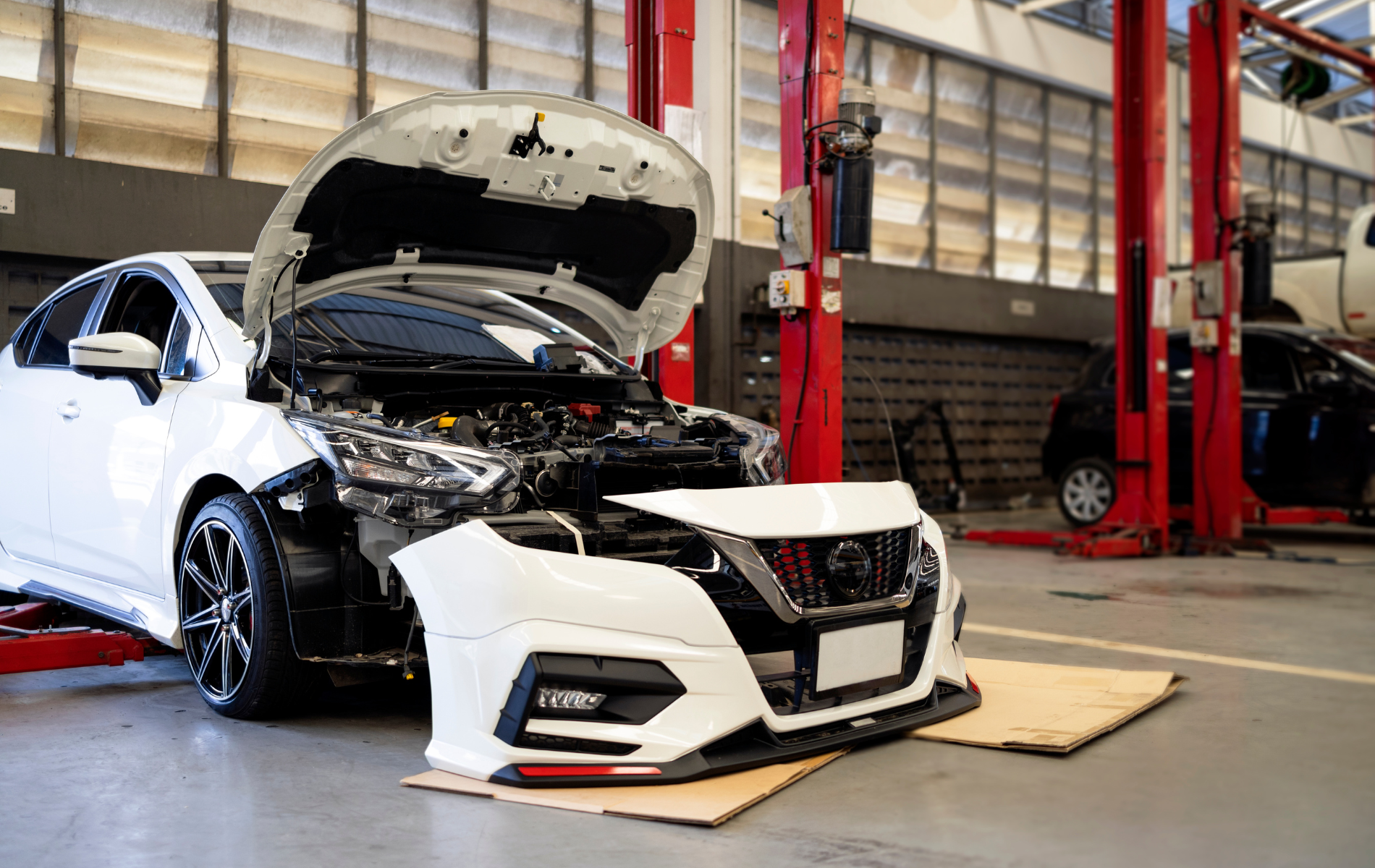 A white car with its hood open is sitting on a lift in a garage.