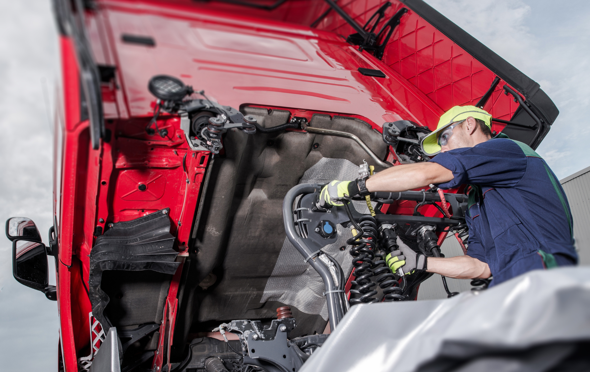 A man is working on the engine of a red truck.