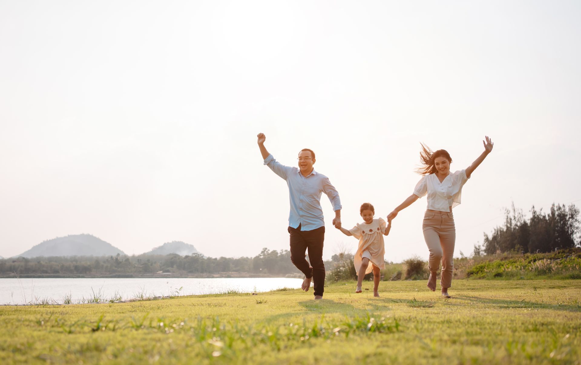 Family running on green grass next to a body of water, arms raised in the air.