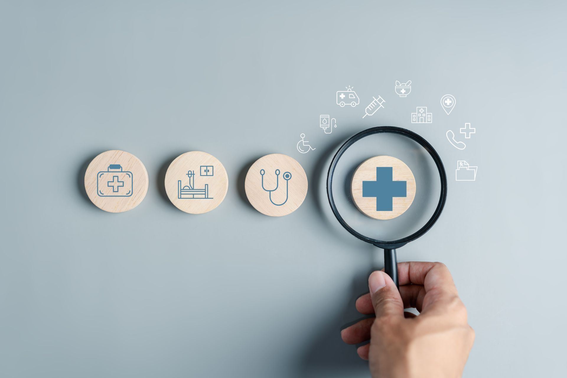 Hand holding magnifying glass over a health icon, next to healthcare symbols.