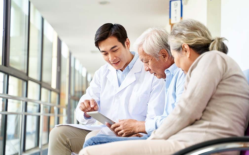 Doctor showing tablet to senior couple in a hallway.