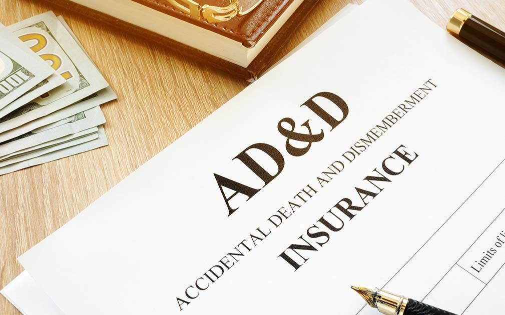 AD&D insurance document with cash, a pen, and a closed box on a wooden surface.