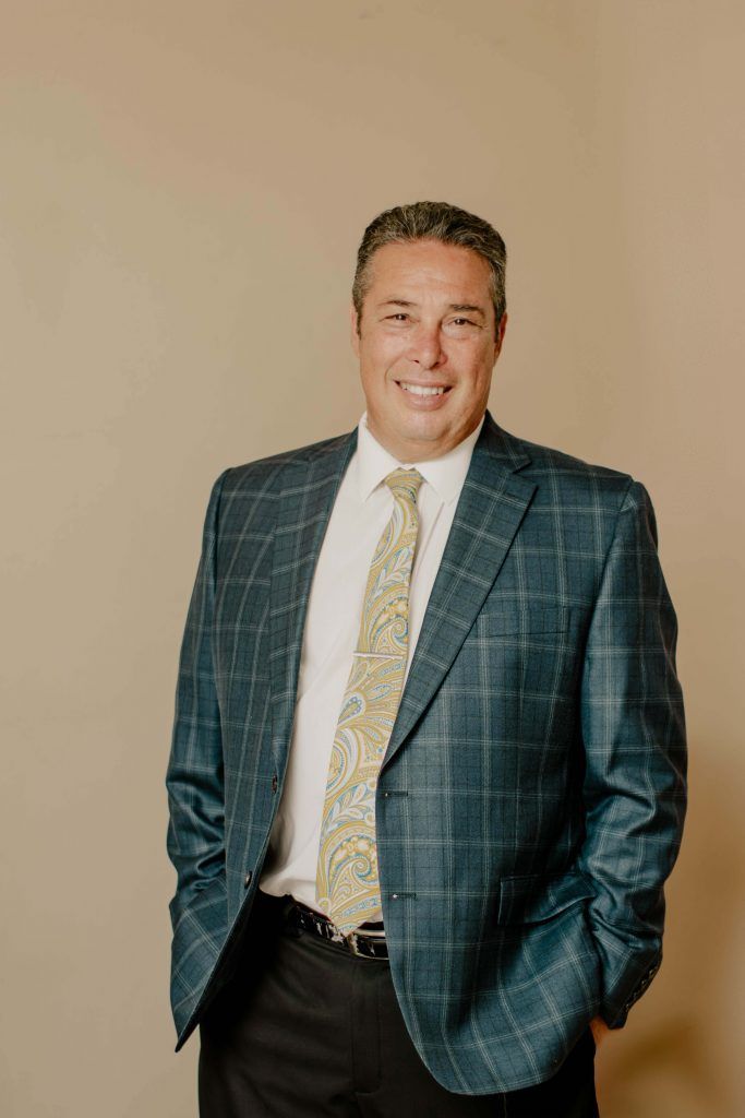 Man in blue plaid blazer, smiling, hands in pockets.