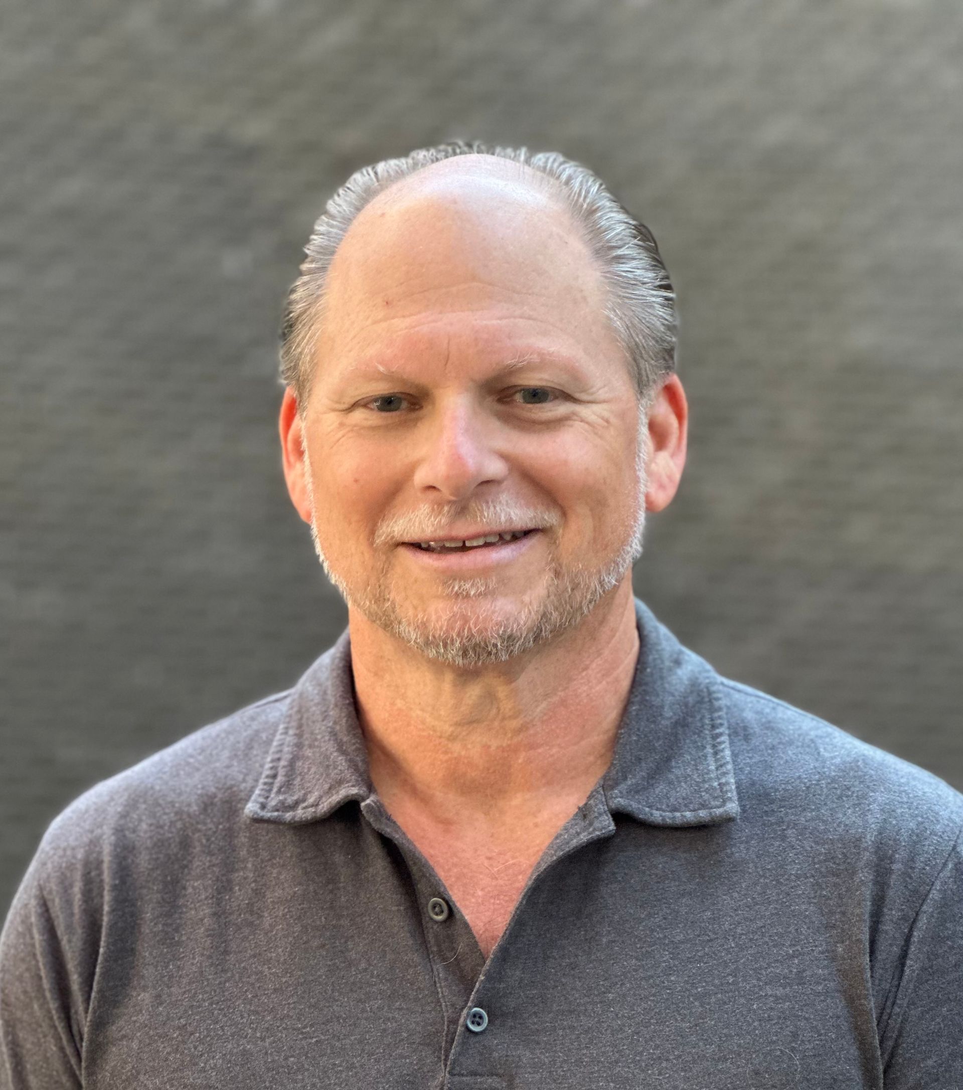 Man with short brown hair, looking at the camera with a neutral expression. American flag in the background.
