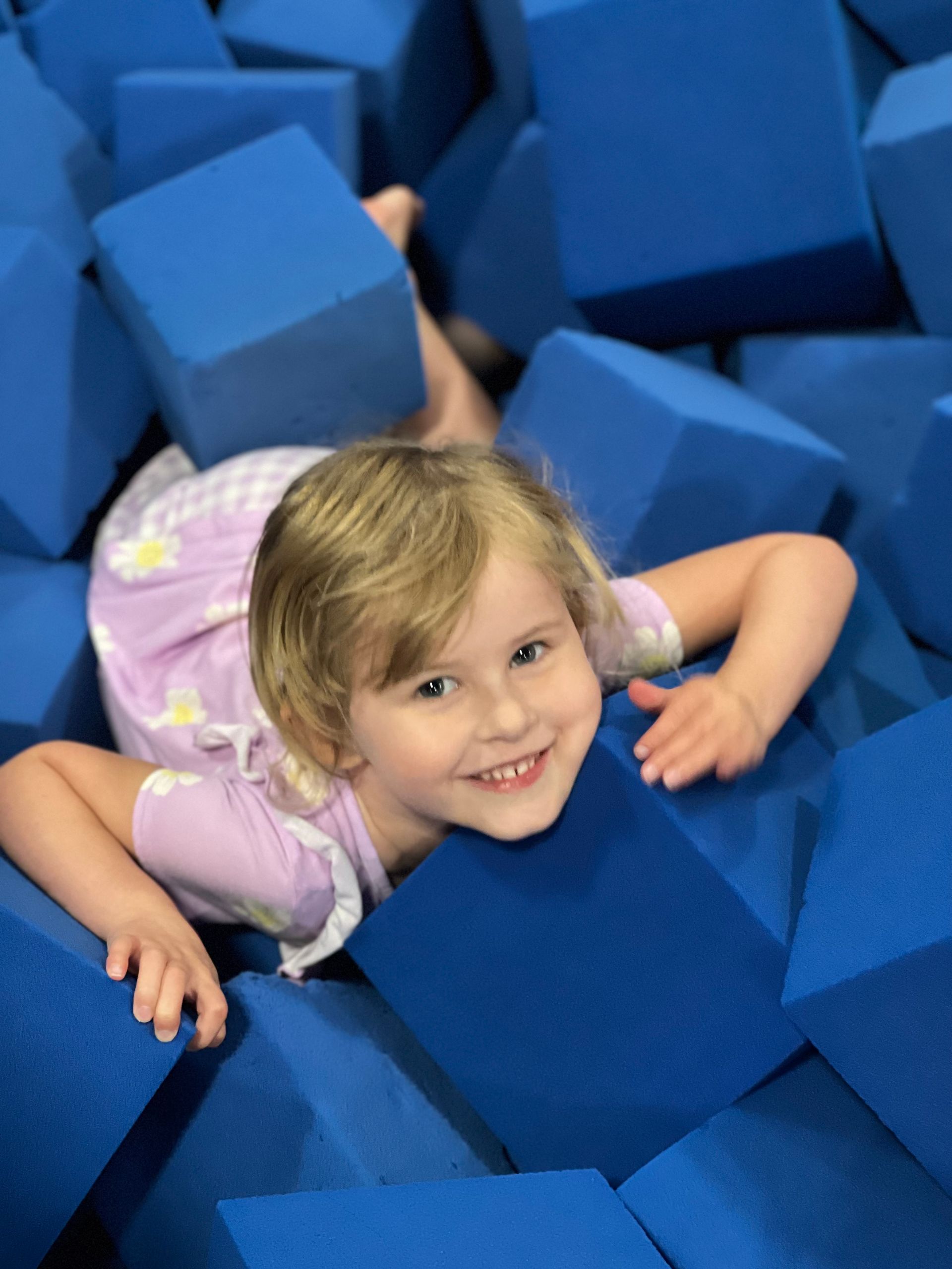 A little girl is laying in a pile of blue foam cubes