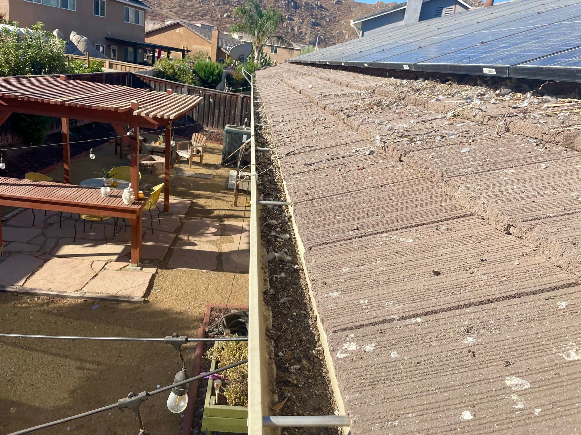 A roof with a gutter on it and a pergola in the background.