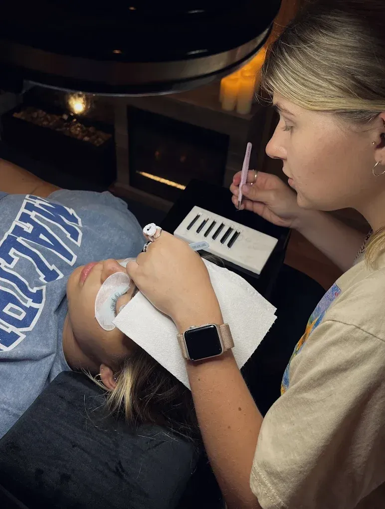 Woman getting eyelash extensions by technician; close-up of eye, tools, and work setup.