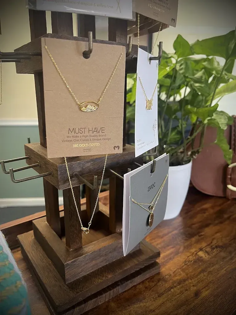 Wooden jewelry display with gold necklaces hanging. A potted plant sits in the background.