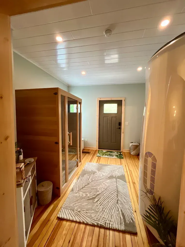 Hallway with wooden sauna and large white pod. Door in background, rug on floor.