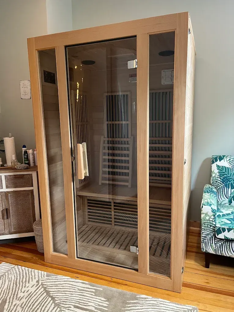 Wooden sauna with glass door and side panels, interior bench, in a room.