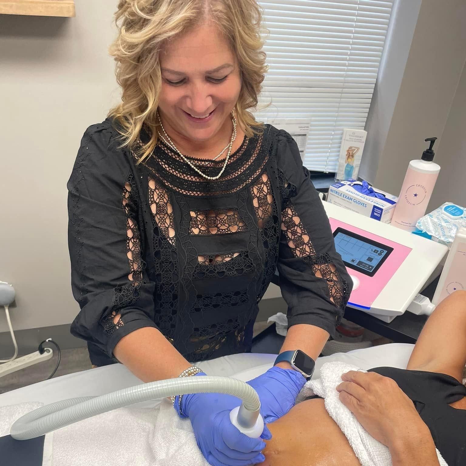 Woman performing body treatment with a device, smiling. Office setting, blue gloves.