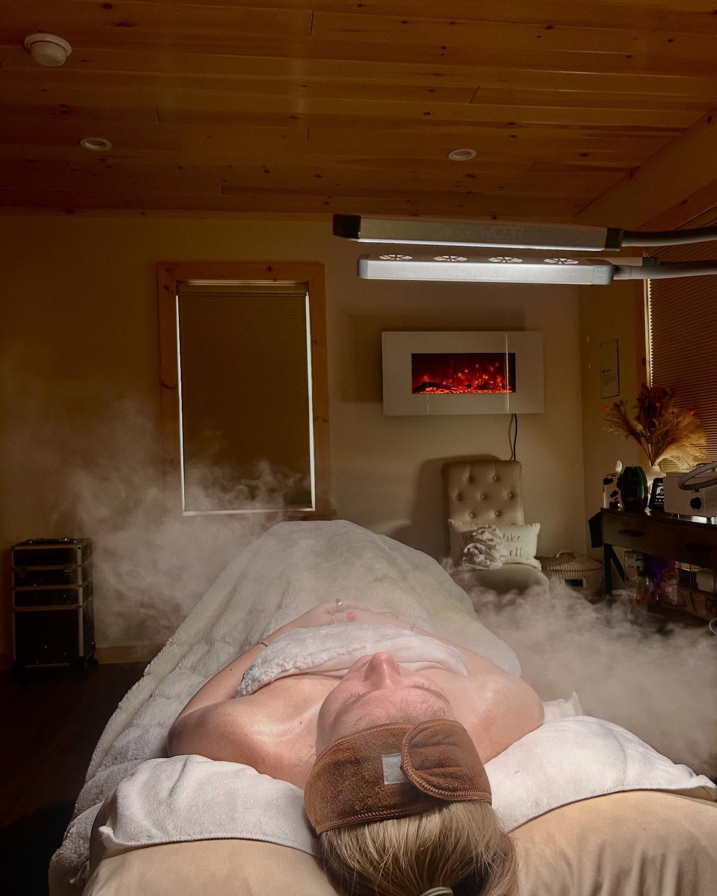 Person laying on massage table, steam rising. Relaxing spa setting with fireplace and lights.