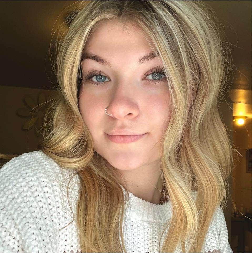 Blonde woman with light blue eyes, smiling, wearing a white sweater.