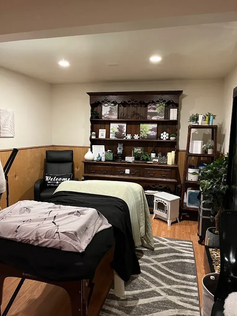 Massage therapy room with massage table, rug, cabinet, and armchair.