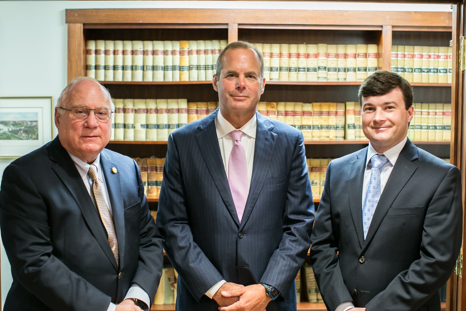 Three men in suits standing in front of a bookshelf filled with books.