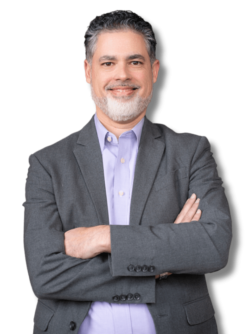 Man in navy suit and pink tie smiles in a library, bookshelves in the background.