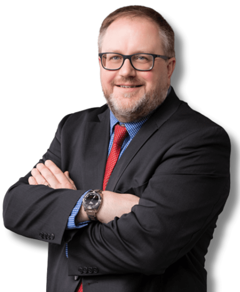 Man in navy suit and pink tie smiles in a library, bookshelves in the background.