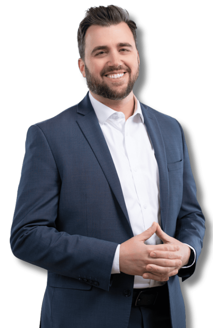 Man in navy suit and pink tie smiles in a library, bookshelves in the background.