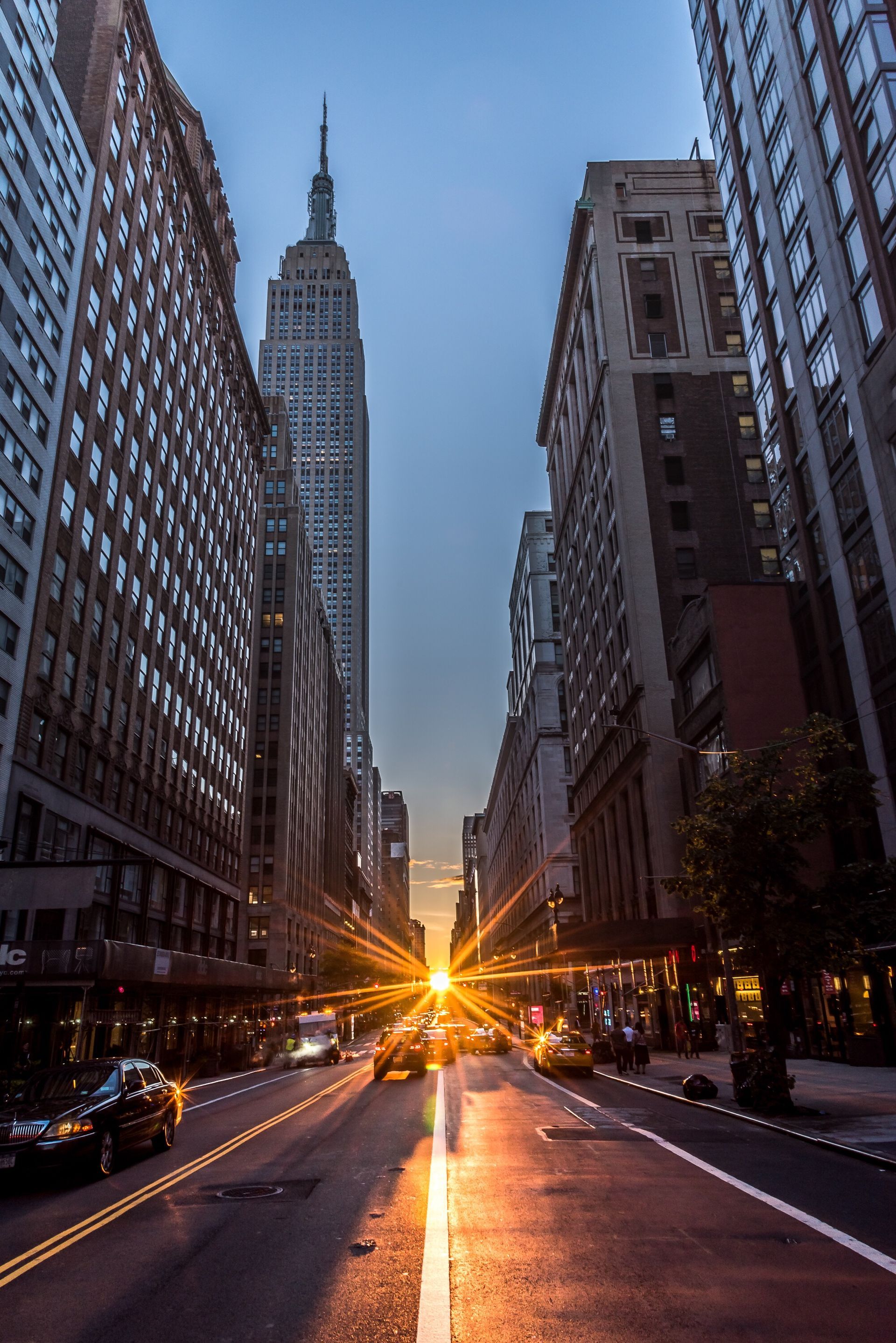 New York City street scene with Empire State Building at the end, sunset with lens flare.