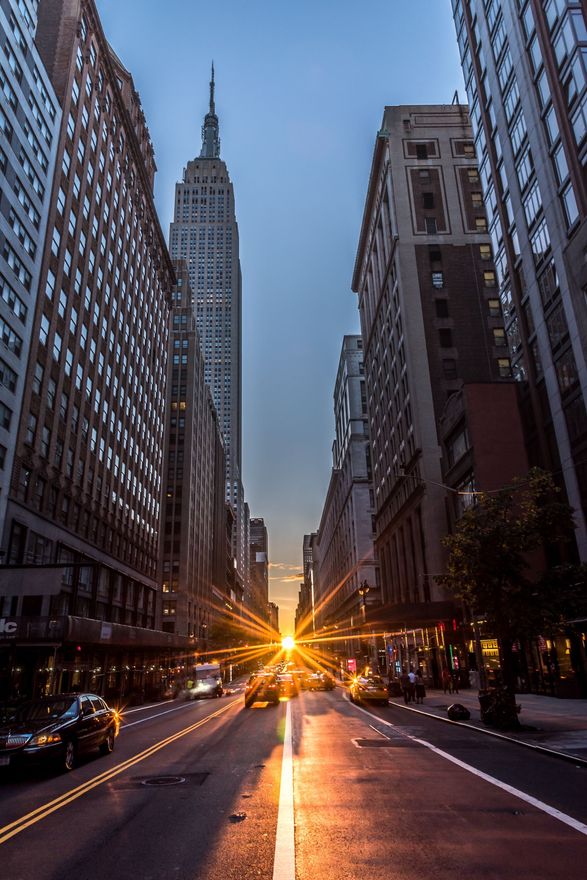 New York City street scene with Empire State Building at the end, sunset with lens flare.