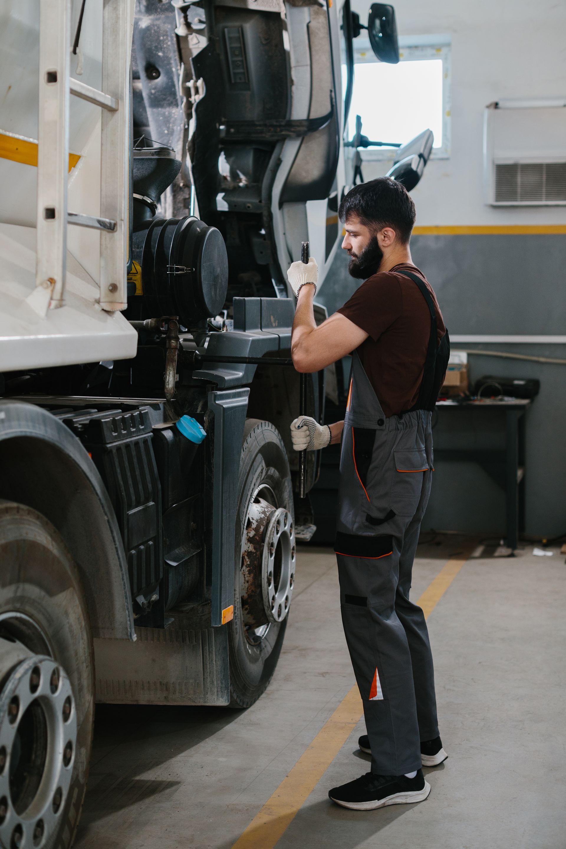 Mechanic in grey overalls inspecting truck tire in a garage.