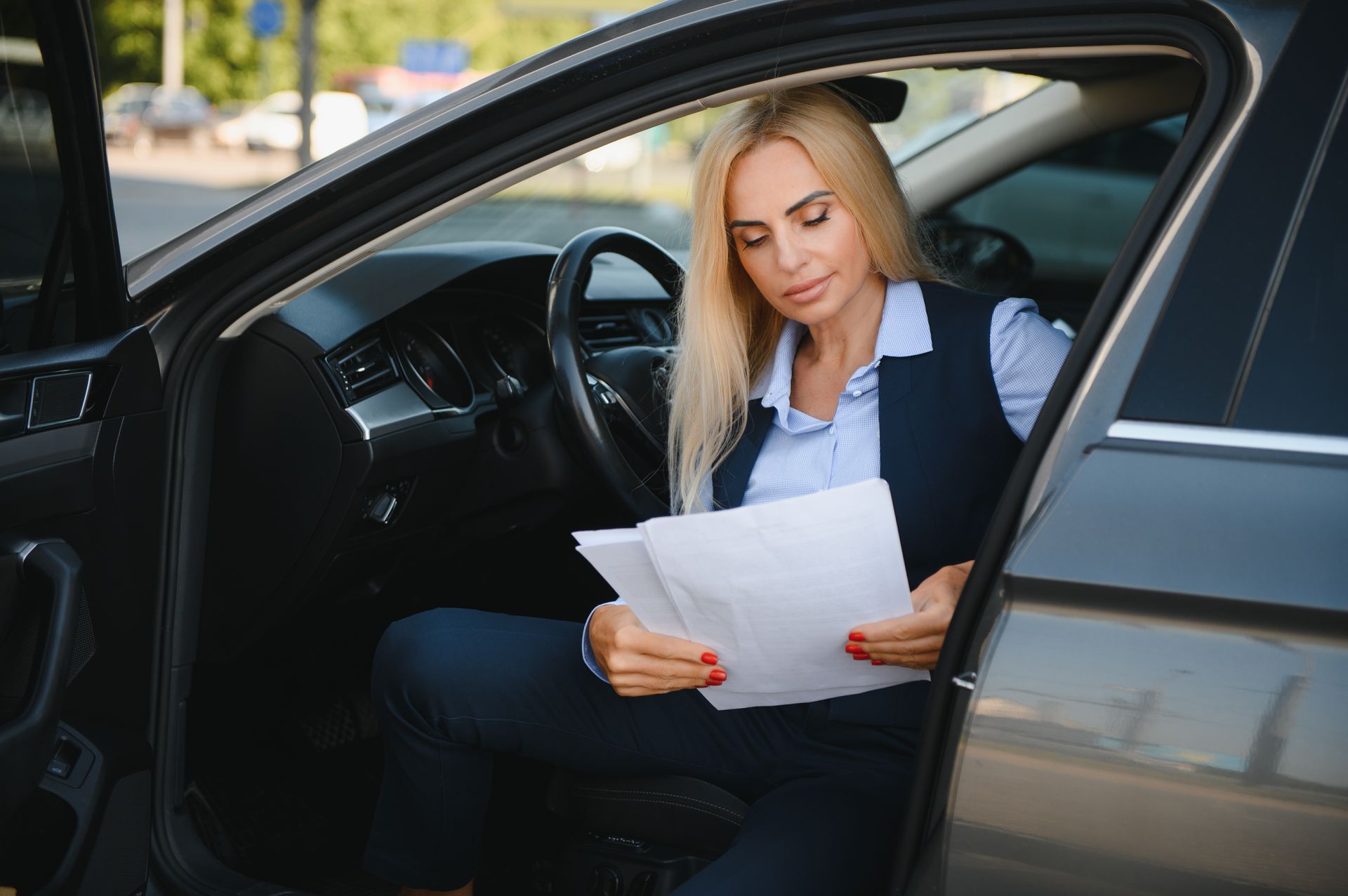 A person sitting in the driver's seat of a car, reviewing documents.