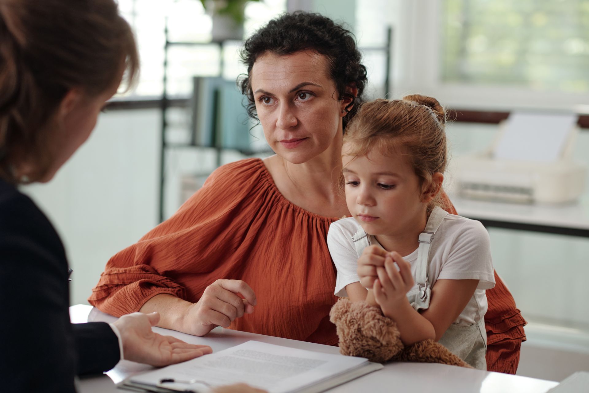 A woman and child sit at a table across from a professional, focusing on documents in an office setting.