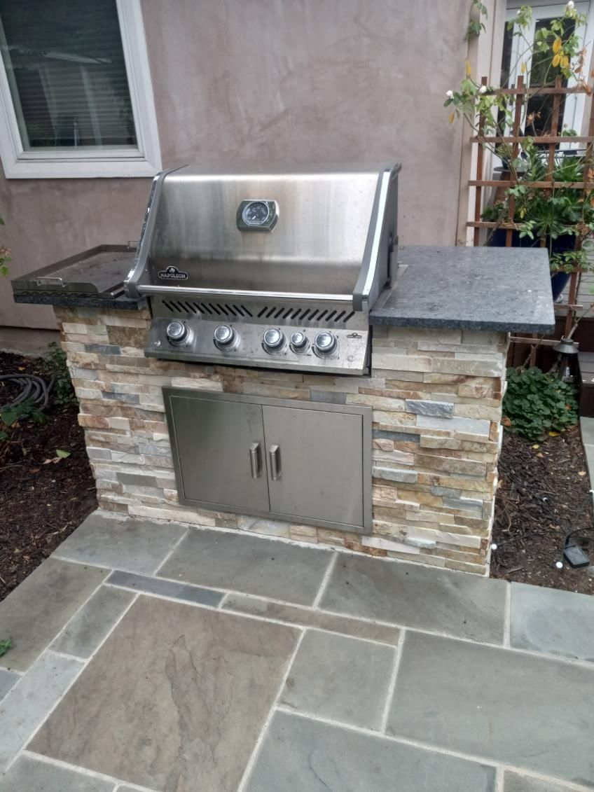Outdoor built-in stainless steel grill with stone base on a patio