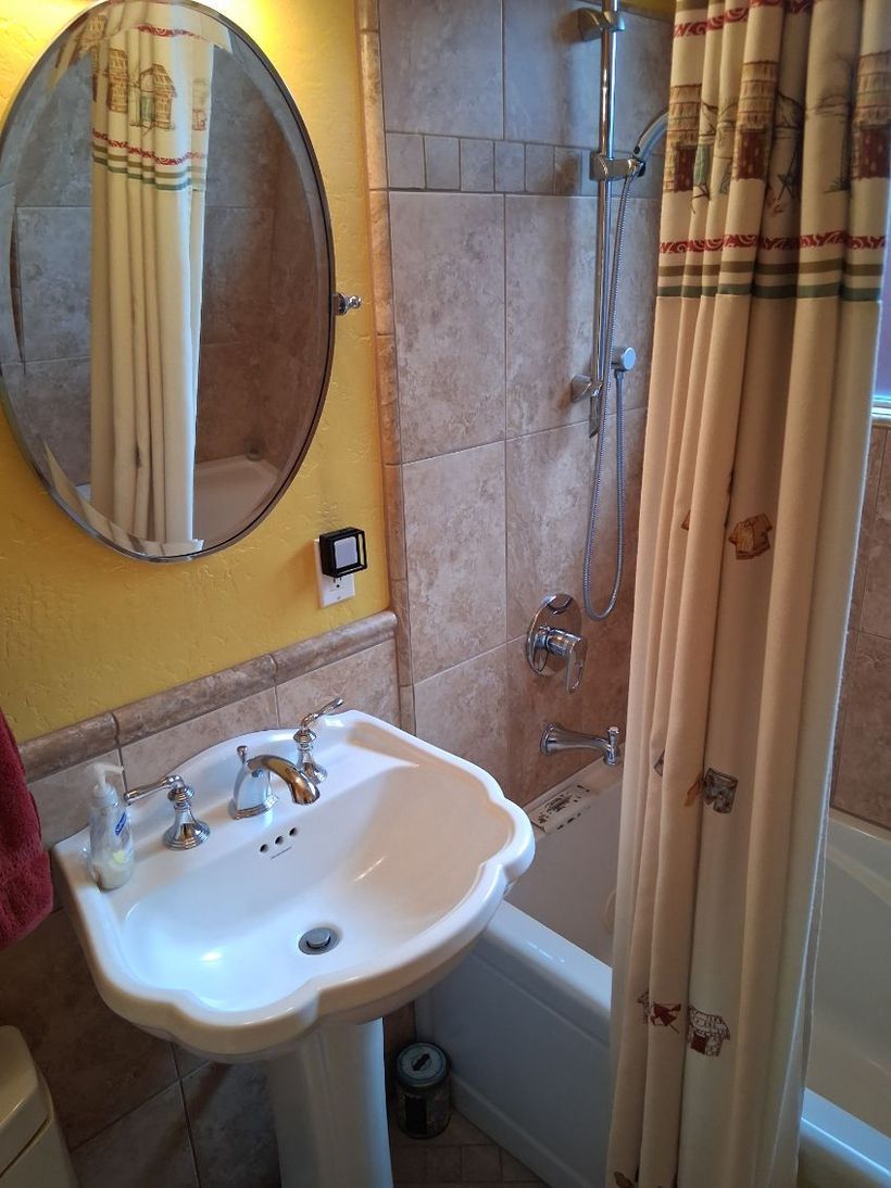 Small bathroom with a sink, oval mirror, glass shower, and yellow walls.