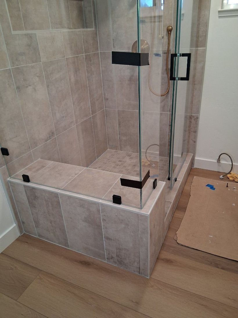 Glass shower enclosure with beige tile walls and wood-look floor in a bathroom renovation